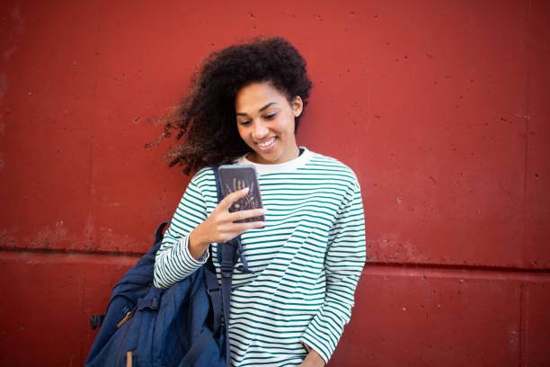 istock smiling young woman standing by wall, looking at mobile phone 1758100402