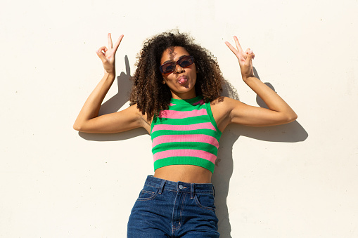 Portrait young woman by white background with tongue out