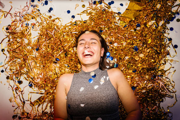 Photo of a young , smiling woman celebrating New Year's Eve, while colourful confetti falling over her during countdown
