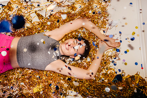 Photo of a young , smiling woman celebrating New Year's Eve, while colourful confetti falling over her during countdown