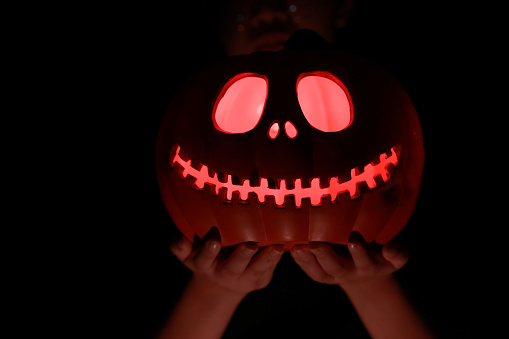 Female hands holding an illuminated pumpkin for Halloween. A  the jack-o'-lantern with the red light inside