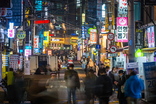 People walking through the neon lit night streets of Sinchon in the heart of Seoul, South Korea’s vibrant capital city.