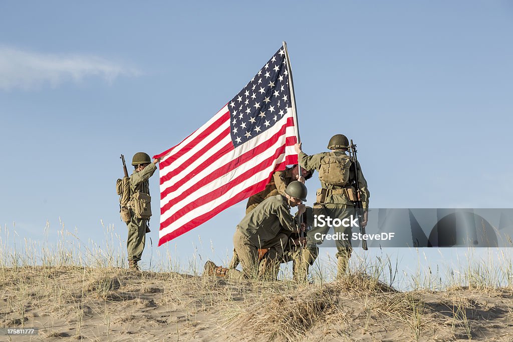 WW2 Soldiers Raising the Flag Four soldiers in authentic US World War II uniforms raise the US flag over the battlefield. Similar to the raising the flag at Iwo Jima. Flag is period appropriate 48 star flag. American Culture Stock Photo