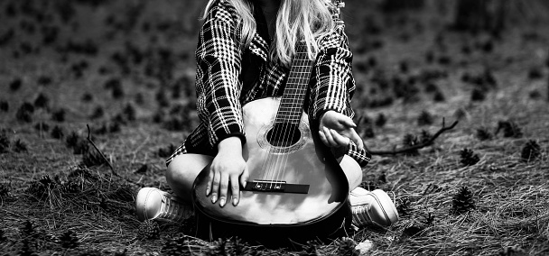 Young girl sitting in the woods with a guitar