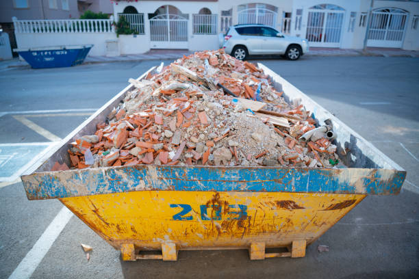 A bright yellow dumpster, marked with the number '208', sits prominently on a suburban street. Filled to the brim, the container is laden with construction debris, including broken bricks, chunks of concrete, and remnants of pipes. These discarded materials speak to the renovation or demolition efforts that might be underway in the nearby vicinity. The backdrop showcases residential houses with white gated entrances, and a parked car is seen just beside the dumpster. The image captures a moment in urban development, where old structures make way for new ones, and the waste becomes a temporary yet telling landmark of change.
