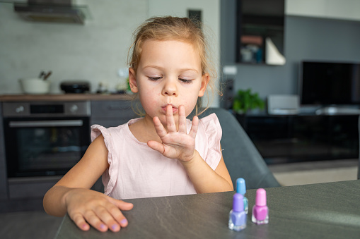 Little girl doing manicure and painting nails with colorful pink, blue and purple nail polish at home. Child girl Blowing on your nails. High quality photo