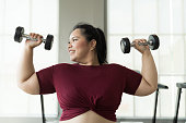 Asian young chubby size woman lifting dumbbells weight in fitness club. Young overweight woman holding dumbbells in workout at gym
