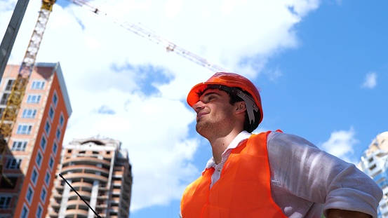 Smiling male builder in helmet holding walkie-talkie while talking, working in construction site. Business, building, industry concept. Slow motion