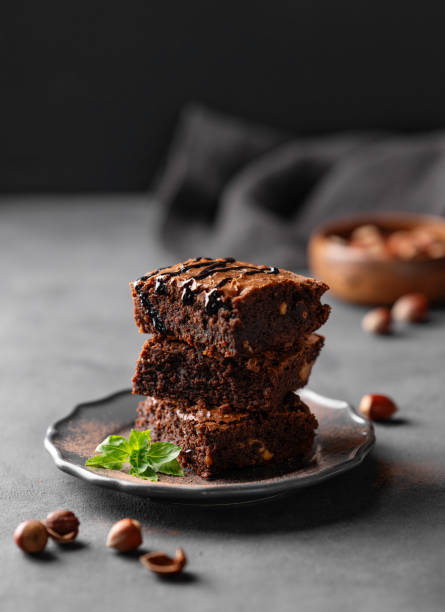 A stack of chocolate vegetarian brownies with mint and  hazelnuts on a dark  background with nuts. The concept of delicious and sweet homemade baked goods.