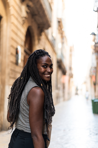 Vertical photo with copy space of an african american woman with braided hair smiling at camera while walking along a narrow street in the city