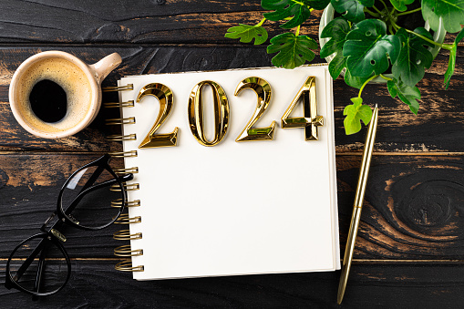 New year resolutions 2024 on desk. 2024 resolutions list with notebook, coffee cup on table. Goals, resolutions, plan, action, checklist concept. New Year 2024 template