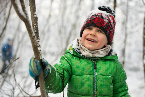 Little boy laughing and shaking snow from trees. The boy is wearing a green jacket and a  knit hat.Shot with Nikon D800