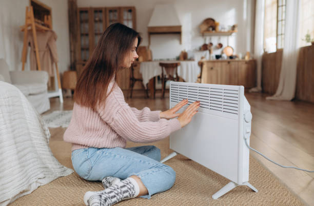 istock Cold home, freezing. Using heater at home in winter. Woman warming her hands sitting by device and wearing warm clothes. Heating season. 1758191365