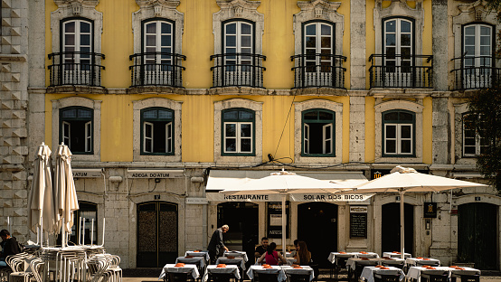 Lisbon, Portugal - May 25, 2023: Facade of a yellow building with a restaurant and the esplanade on the ground floor. High quality photo