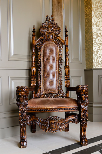 An old, intricately carved oak wood chair with leather upholstering in a house.