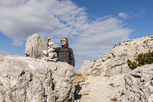 Gray-haired long-haired man building a tower of stones against the background of a picturesque sky and a rocky mountain, Austria. High quality photo