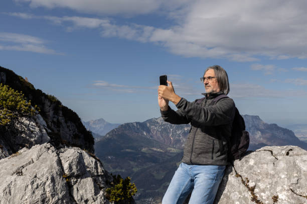istock Gray-haired long-haired man with backpack taking selfie on steep slope on picturesque mountain background, Austria 1758239213