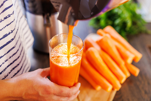 A woman pours fresh carrot juice into glass. Freshly squeezed carrot juice using a juicer