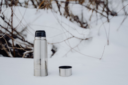 The thermos stands on the snow. Metal dishes vacuum. Hot coffee is brewed in a thermos. Winter cold photo. High quality photo