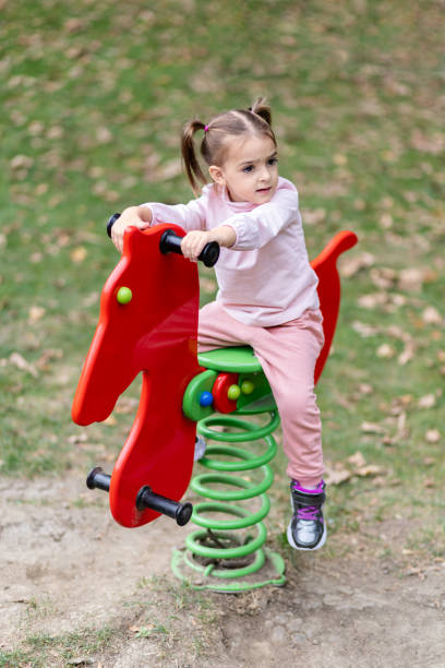Young happy girl riding rocking horse at the park. Portrait of cute girl playing on bouncy horse at the playground. playground spring horse stock pictures, royalty-free photos & images