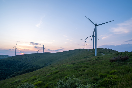 A group of wind turbines on a mountain ridge at sunset.