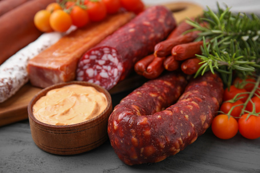 Different types of tasty sausages on grey wooden table, closeup