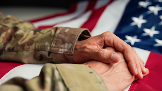 Handshake between enlisted military member and a female civilian. Shot against an American flag. Selective focus on hands.