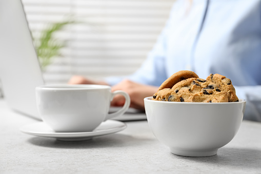 Chocolate chip cookies with cup of drink on table and office worker on background, closeup