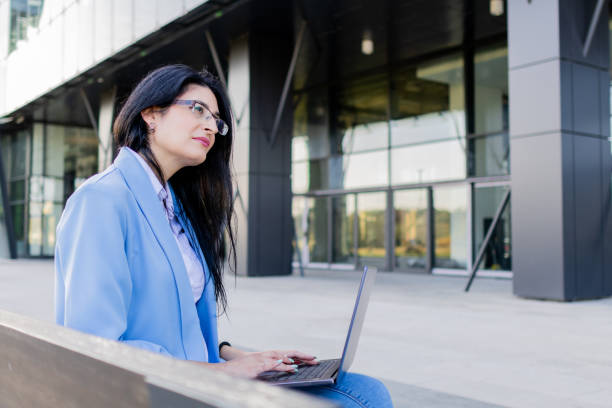 istock Young beautiful businesswoman is using laptop outside. She is studying online or working on the Internet. Concept of online communication, internet technology, online business. 1758344896