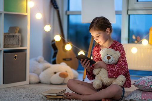 Pretty little girl with smartphone in night room