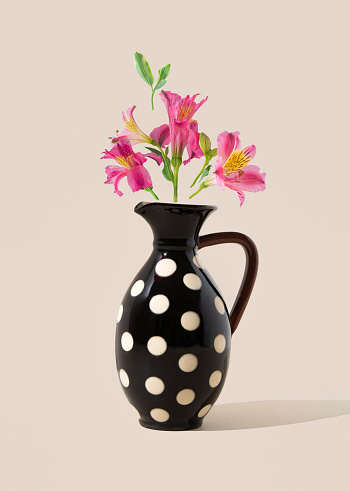 Wild lily flowers levitate above black vase with polka dots. Front view. Greeting card.