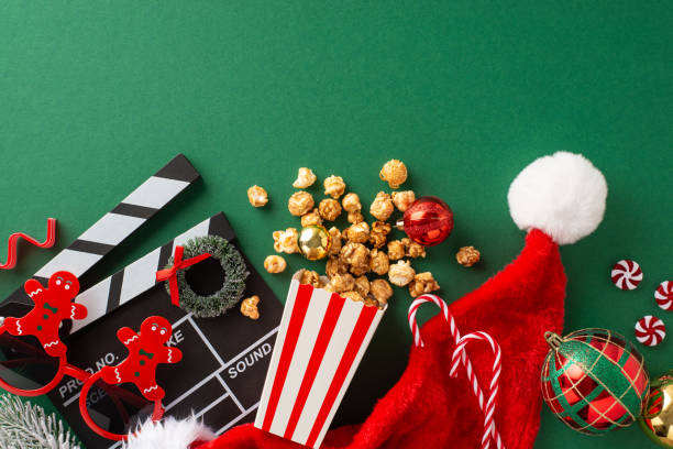 Family-oriented New Year's debut with children's theme. Top view of clapper, gingerbread man-inspired glasses, popcorn in paper box, Santa's hat, balls, wreath, sweets on green backdrop with ad space debut de año nuevo orientado a la familia con temática infantil. vista superior del badajo, vasos inspirados en el hombre de jengibre, palomitas de maíz en una caja de papel, sombrero de papá noel, pelotas, corona, dulces sobre fondo verde con espacio