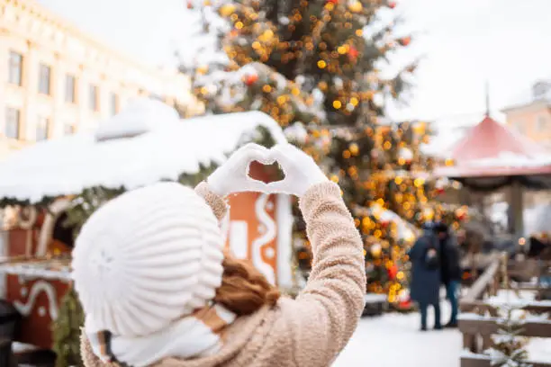 Photo of Young woman holding hands in the shape of a heart against the background of a Christmas tree.