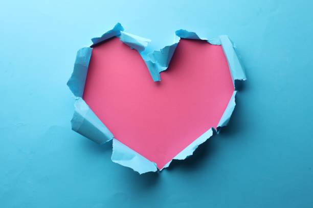 istock Torn heart shaped hole in light blue paper on pink background 1758411321