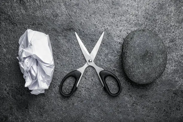 Photo of Rock, crumpled paper and scissors on dark grey textured table, flat lay