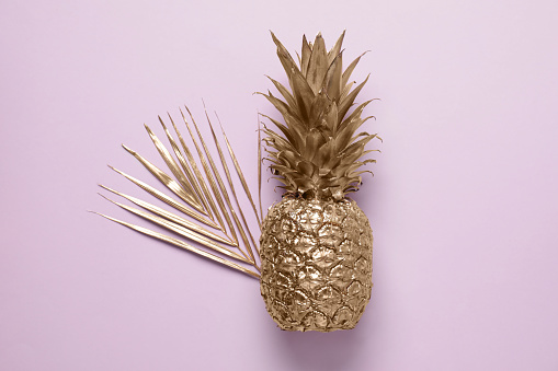Golden pineapple and palm leaf on pink background, top view