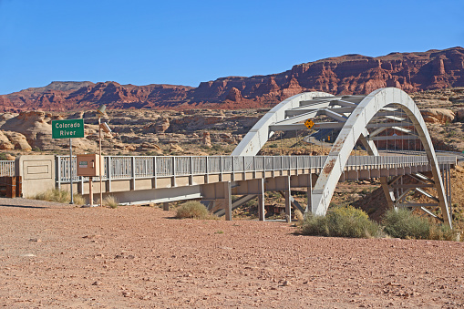 Colorado River sign at the Hite Crossing Bridge for Utah State Route 95 with the Brown Rim cliffs in the background.