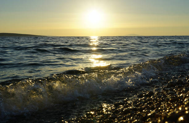 Flooding sea wave splashing on the pebble beach and everything is sparkling in sunshine