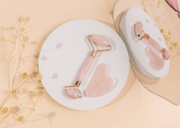istock Facial roller from crystal rose quartz and massage tool jade on beige background with dry flowers. Tools for anti-age massage, natural face lifting at home. Mock up 1758429097