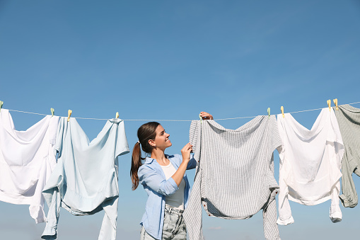 Woman hanging clothes with clothespins on washing line for drying against blue sky
