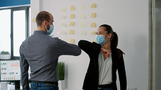 Coworkers with face mask touching elbow with his collegue to prevent infection with coronavirus. Coworkers respecting social distancing while working on communication company project