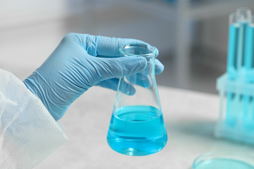 Scientist with beaker of light blue liquid in laboratory, closeup