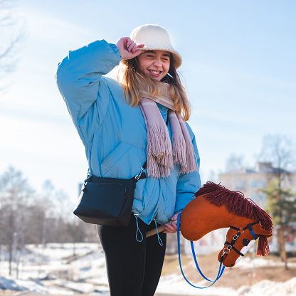Young woman poses with a toy horse on a stick in a city park in winter.