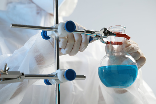 Scientist working with flask of light blue liquid on grey background, closeup