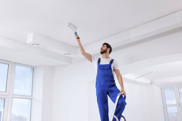 istock Handyman painting ceiling with roller on step ladder in room 1758533242