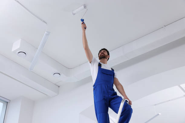 istock Handyman with roller painting ceiling on step ladder in room, low angle view 1758533246