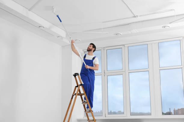 istock Handyman painting ceiling with roller on step ladder in room 1758533771