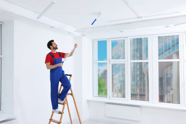 istock Handyman painting ceiling with roller on step ladder in room 1758533773