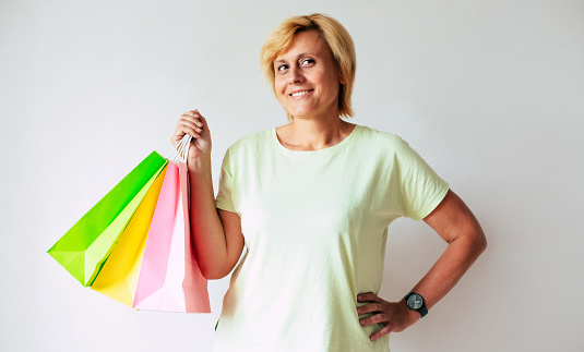 Close up photo of happy mature middle aged woman holds colorful shopping bags at home. Online shopping. Customer payment wireless shopping discount