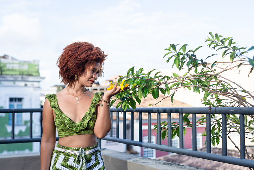 Beautiful woman with red hair, standing touching natural flowers of yellow color. Happy person traveling.